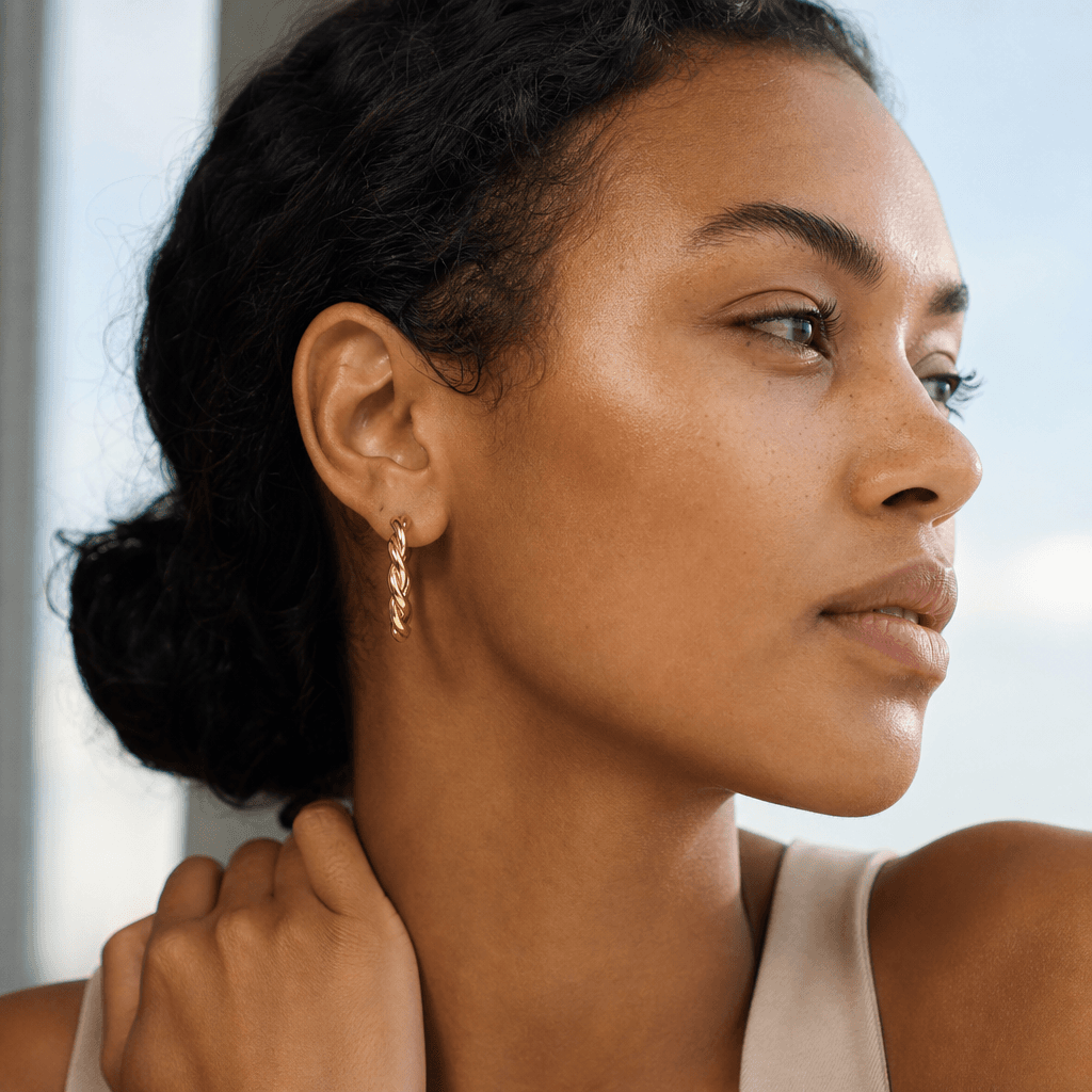 Person wearing twisted solid gold hoop earrings.