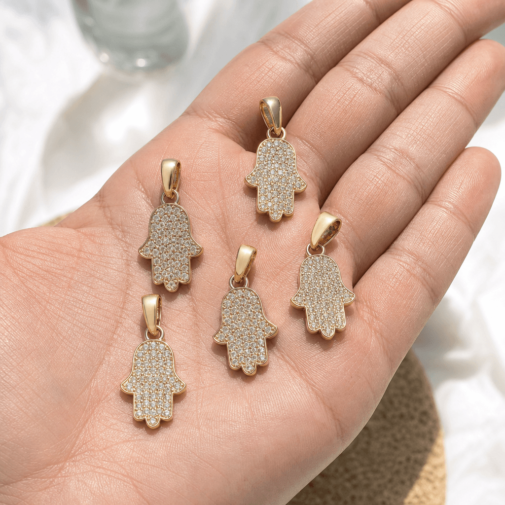 A fan of pavé solid gold hamsa pendants held in hand.